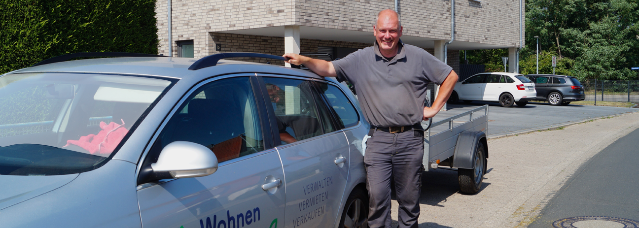Der Mitarbeiter Carsten Rösner von Wohnen und Leben steht lächelnd neben dem Arbeitsauto